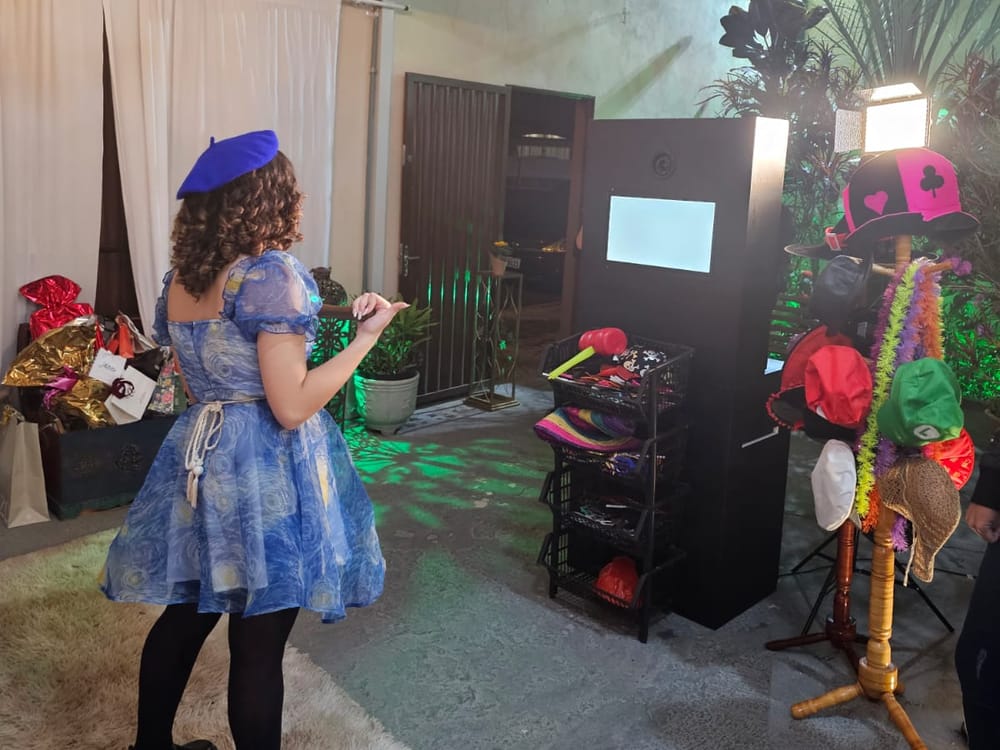 Convidada fantasiada posando na cabine fotográfica, com chapéus e acessórios ao lado
