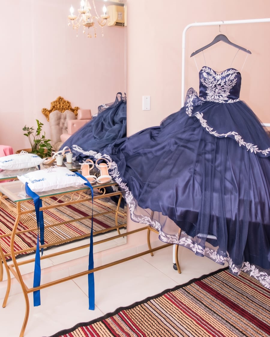 Sala reservada com vestido de debutante na arara, espelho, lustre e sapatos sobre a mesa