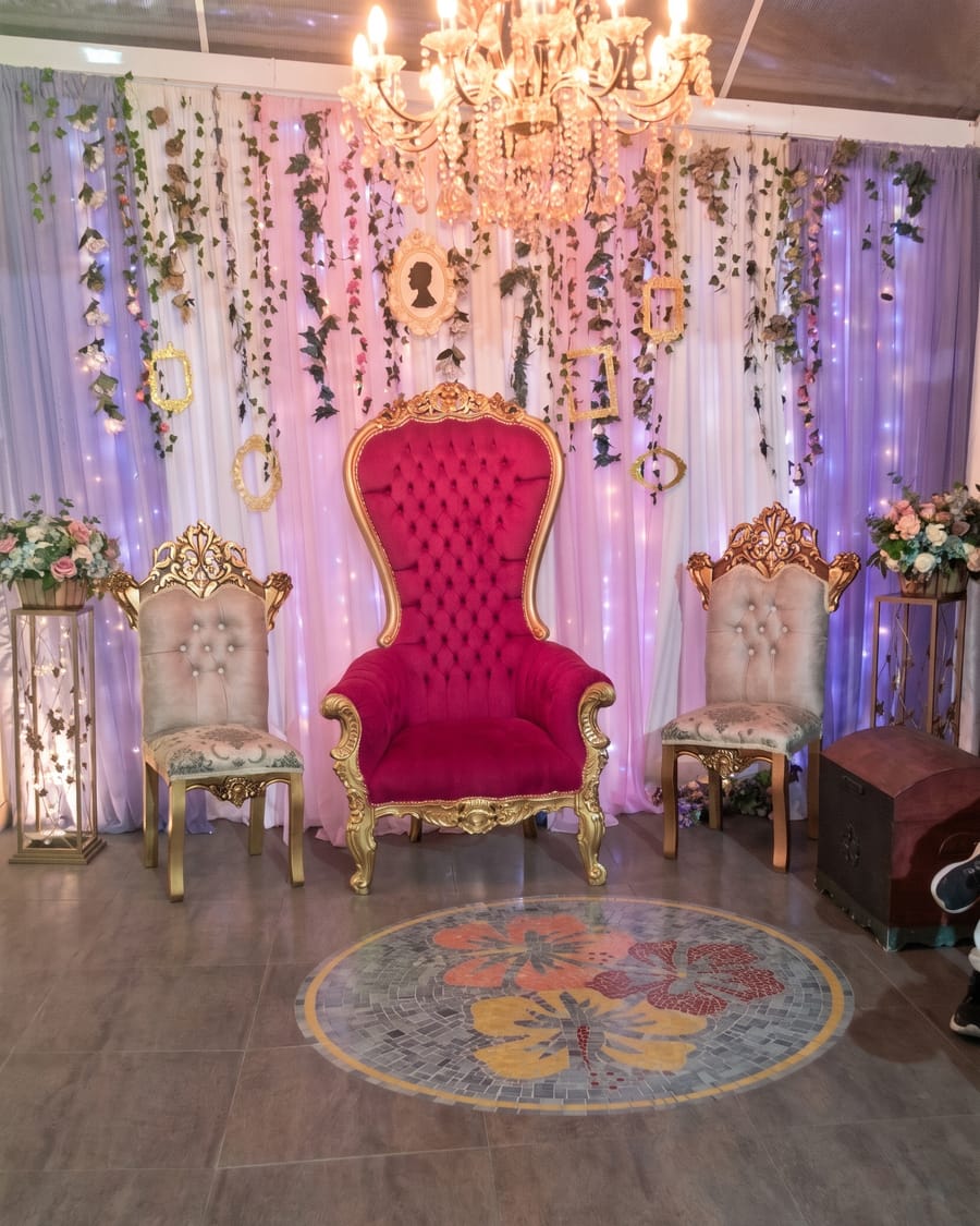 Trono vermelho e dourado diante da cortina de flores, com o mosaico de hibisco no piso do salão